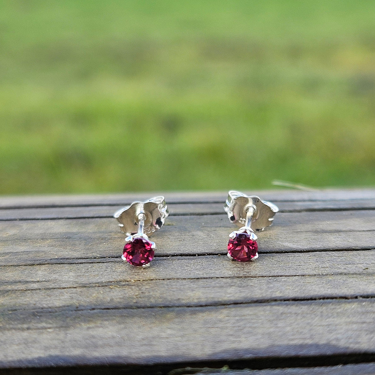 Pair of silver earrings with red gemstones on a wooden surface
