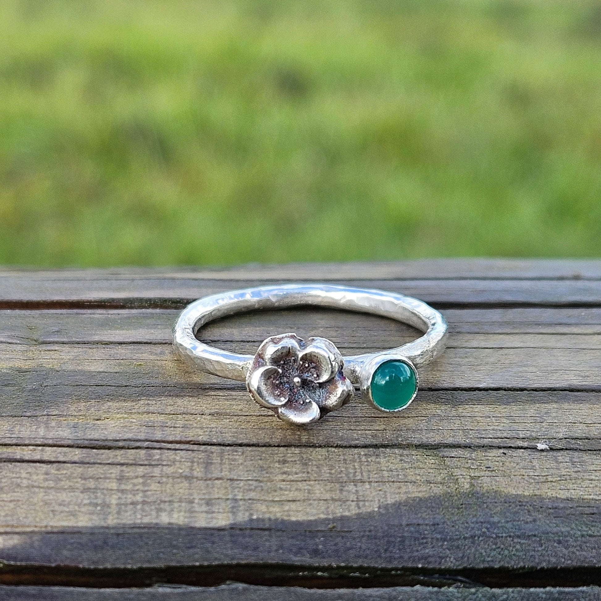 Silver ring with a green gemstone on a wooden surface with a grassy background