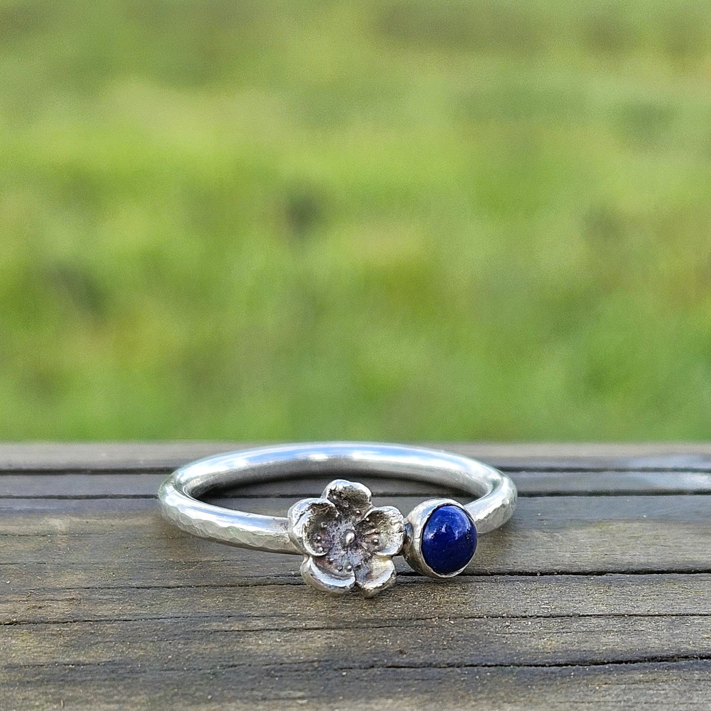 Silver ring with a blue gemstone on a wooden surface with a grassy background
