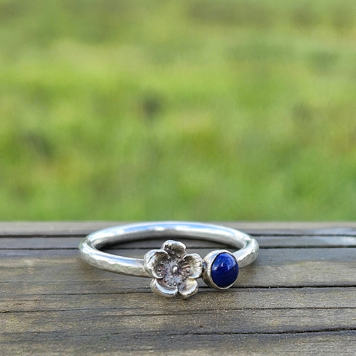 Silver ring with a blue gemstone on a wooden surface with a grassy background